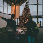 Young couple observes Christmas tree inside airport terminal. Book Holiday Flights