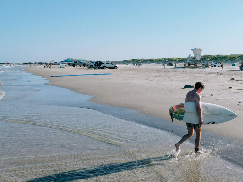 Surfer walking along a Padre Island Beach among the Best Shelling Beaches