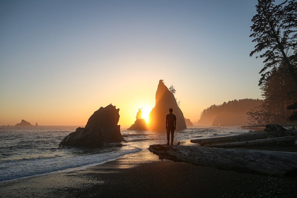 Silhouetted figure observes a breathtaking sunset over Rialto Beach, Washington.